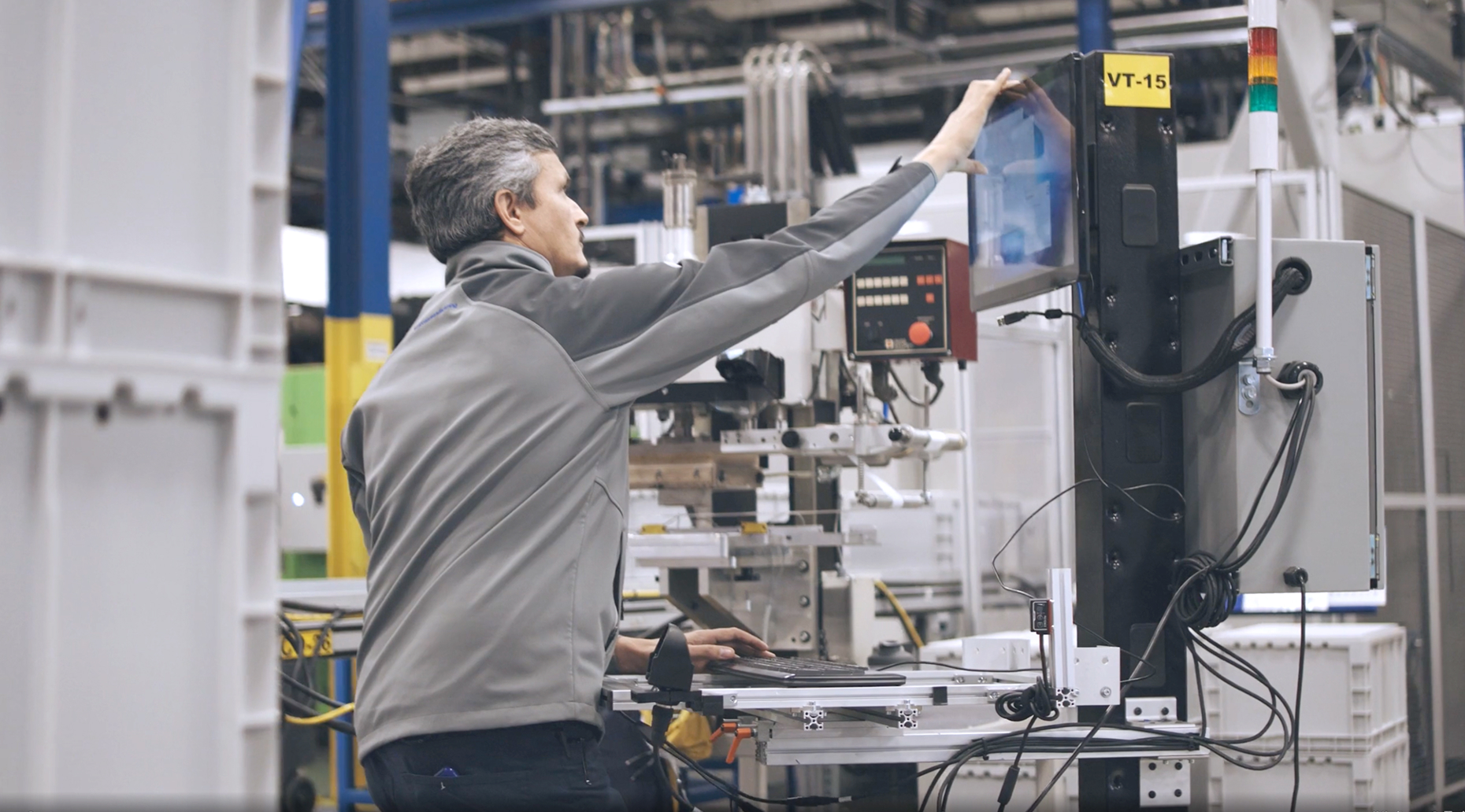 Factory technician operating a touchscreen control panel on industrial machinery inside a manufacturing facility.