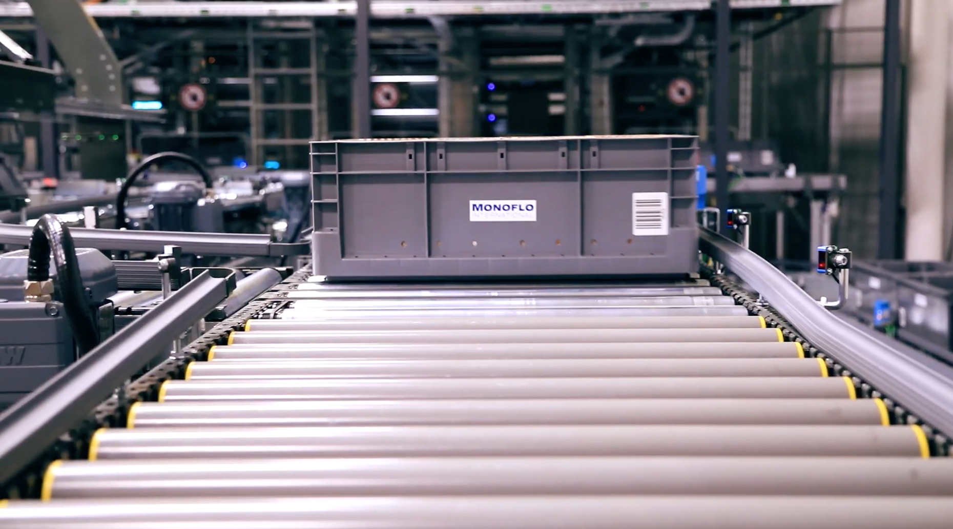 Gray Monoflo automation container moving along an automated conveyor system inside a manufacturing facility.