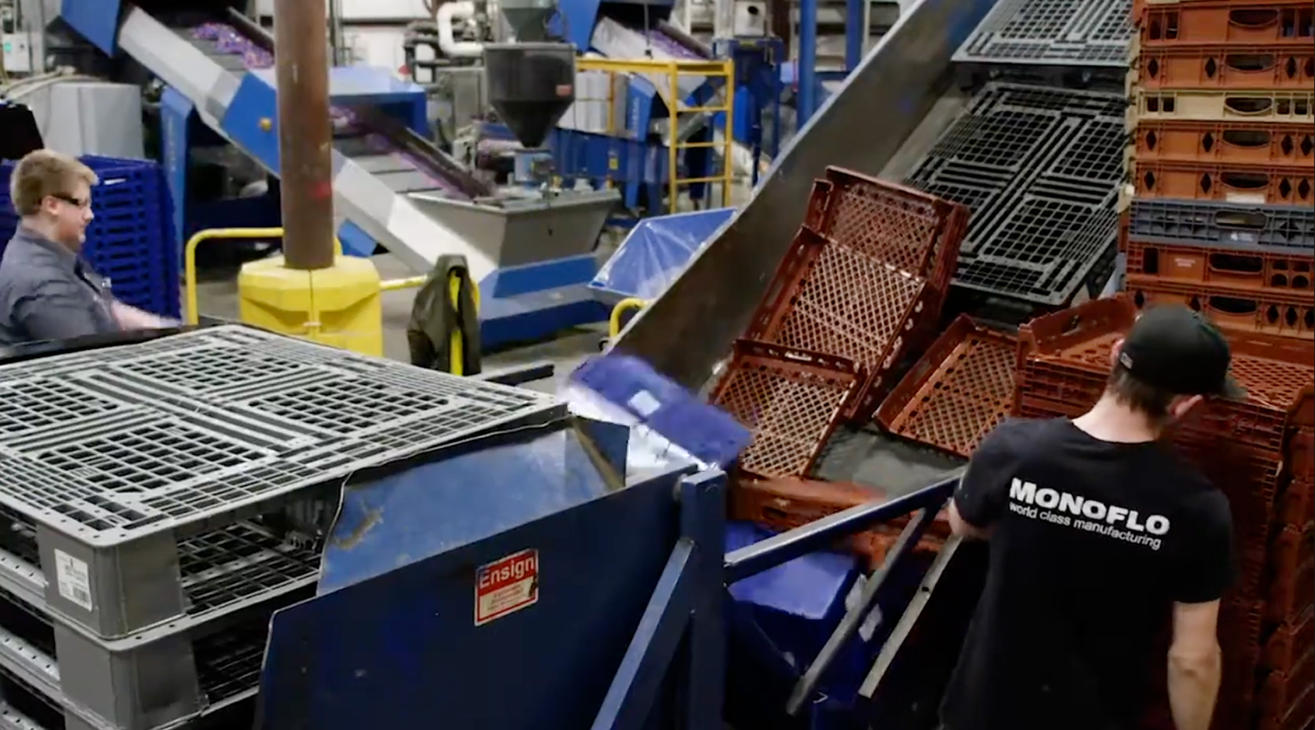 Workers sorting and loading used plastic crates onto a conveyor in a recycling and reprocessing facility.