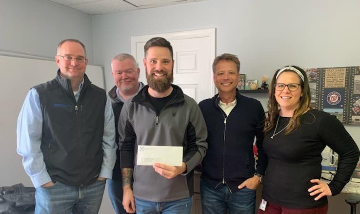 Five individuals in a room proudly holding a large check for Monoflo International's support of the Winchester Rescue Mission 2020.