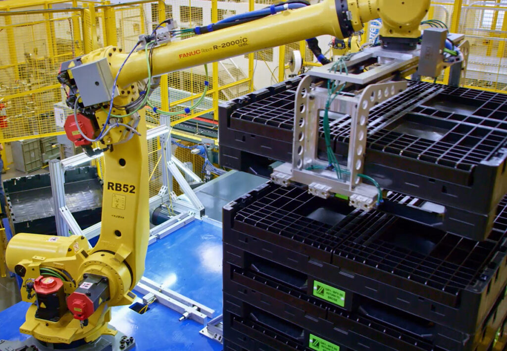 A robotic arm lifts a box from a conveyor belt, showcasing Monoflo International's innovative Bulk Container redesign.